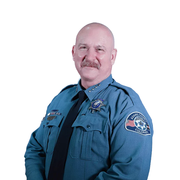 A man in a blue police uniform, smiling, wearing an Adams County badge.
