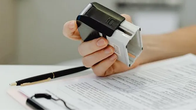 Hand holding a stamp over a document with text, pen nearby
