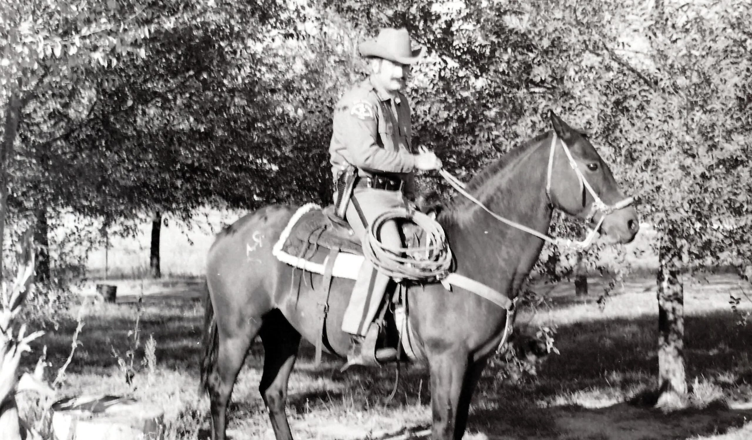 Sheriff on horseback in cowboy hat riding a horse in a wooded area.