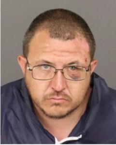 Martinez Alex Anthony with visible facial injuries, wearing glasses and a dark jacket.