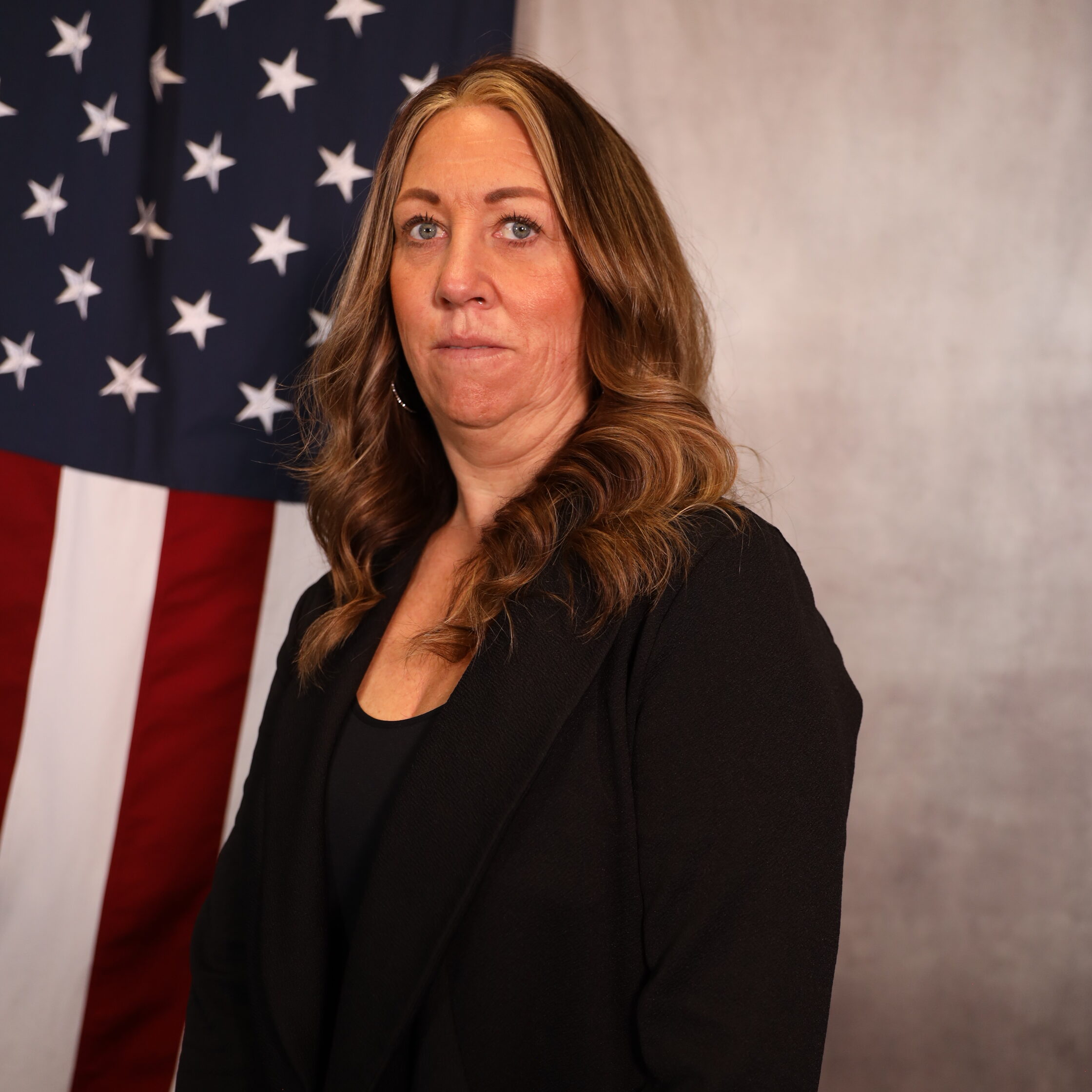 Jana Colwell standing in front of an American flag, wearing a black blazer