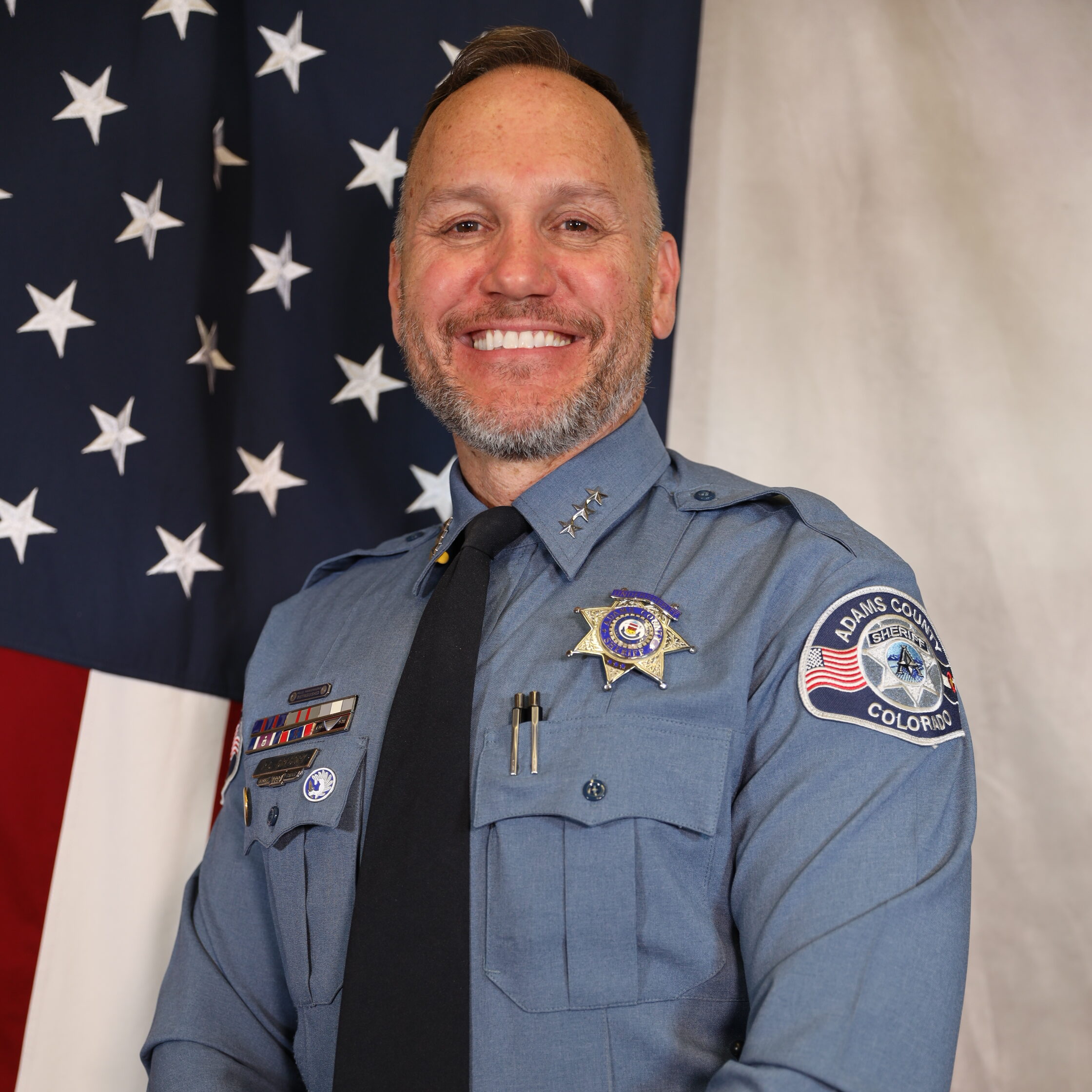 Gregory-Paul in uniform smiling, standing in front of American flag