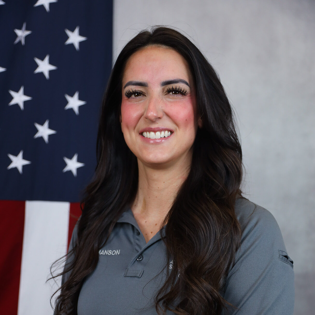 Jesseca Olivas smiling in front of the American flag, wearing a gray shirt