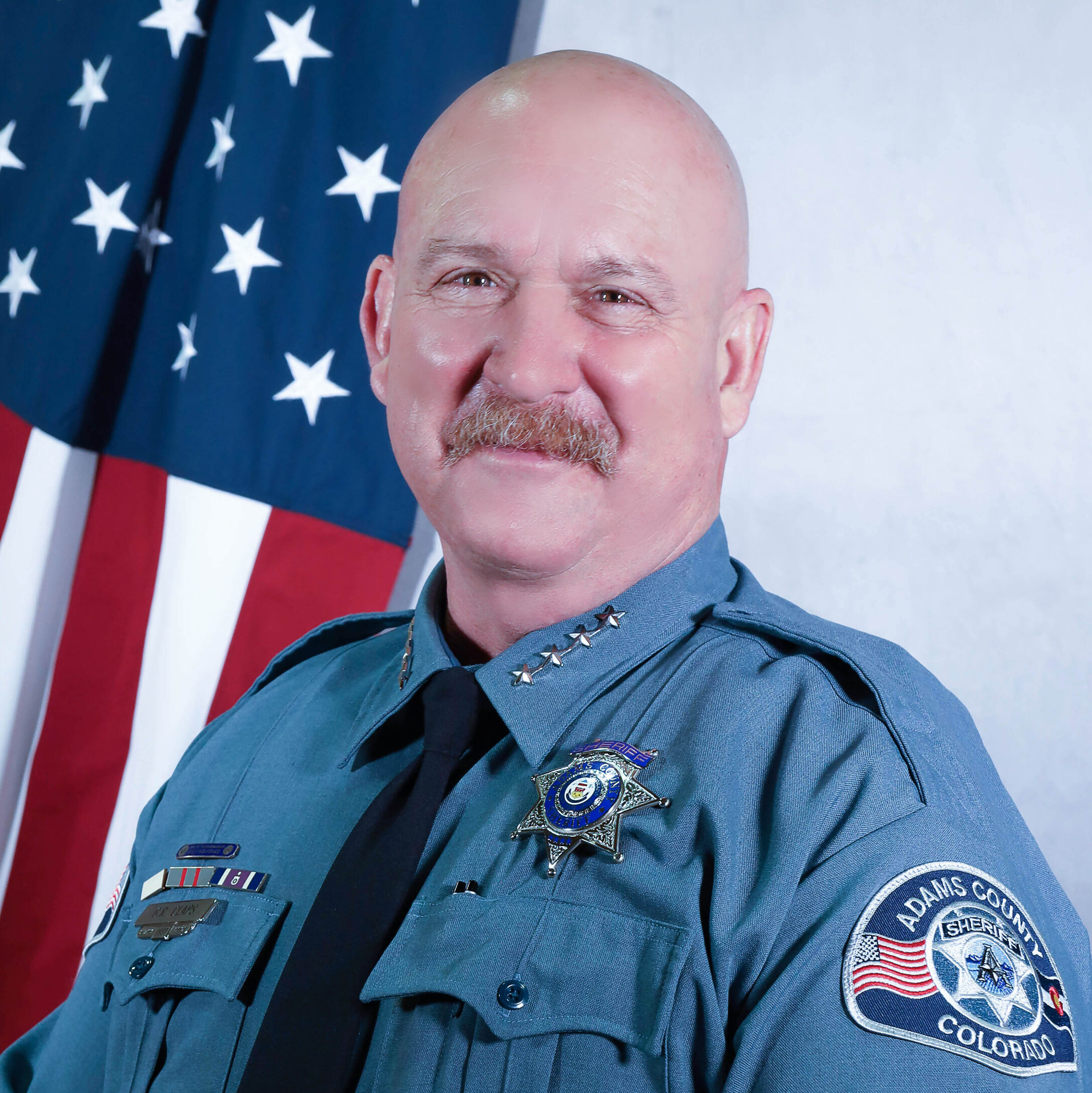 Sheriff Gene Claps in uniform standing in front of the American flag