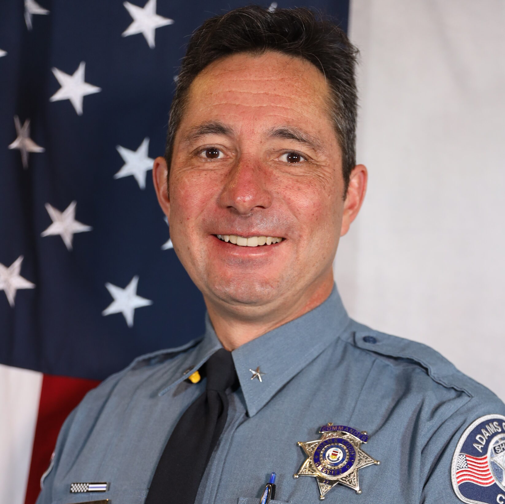 Bitterman-John smiling in uniform, standing in front of the American flag.