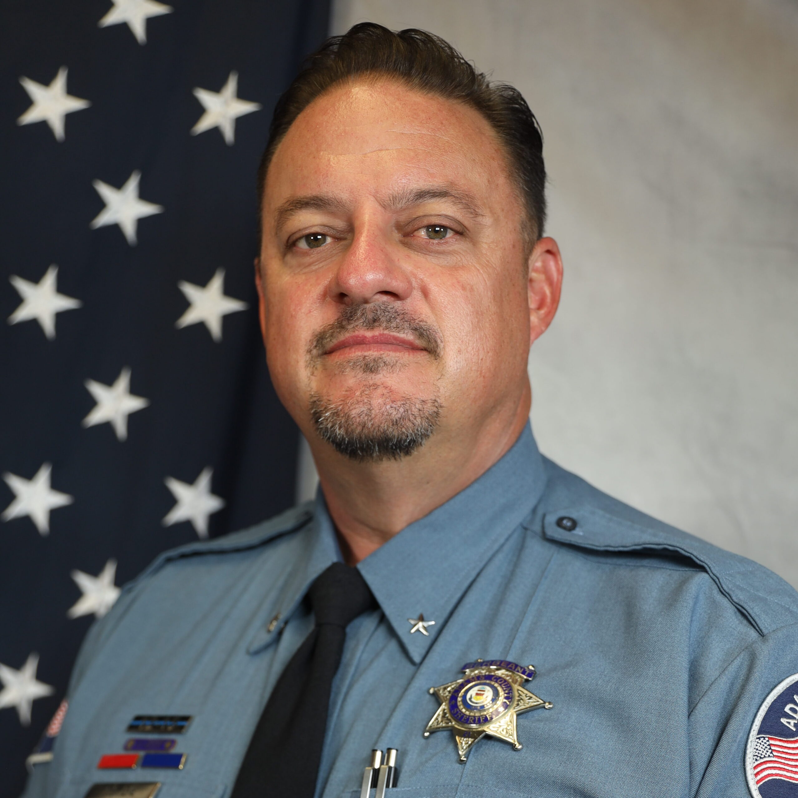 Man in Adams County sheriff uniform stands in front of American flag