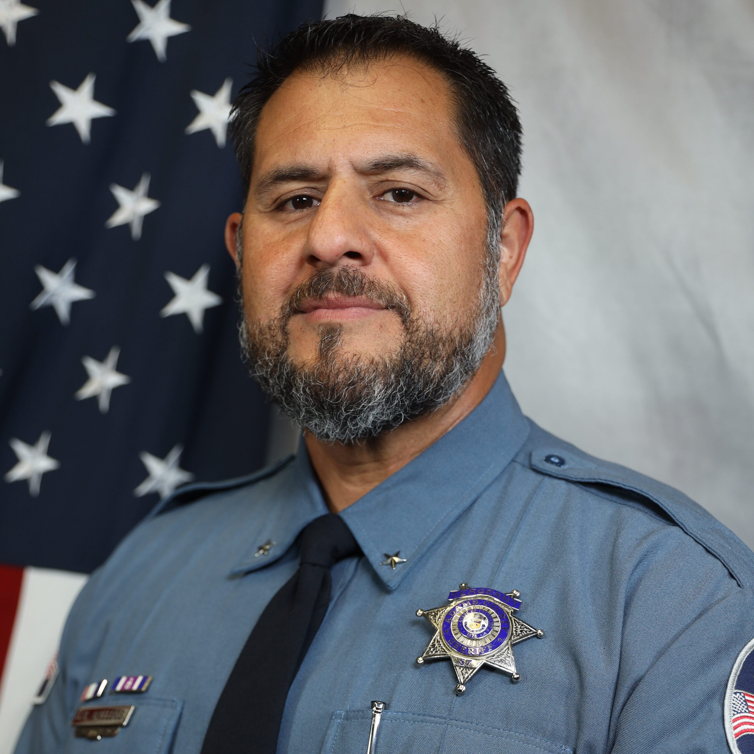 Jason Gallegos, in uniform with badge, standing before U.S. flag