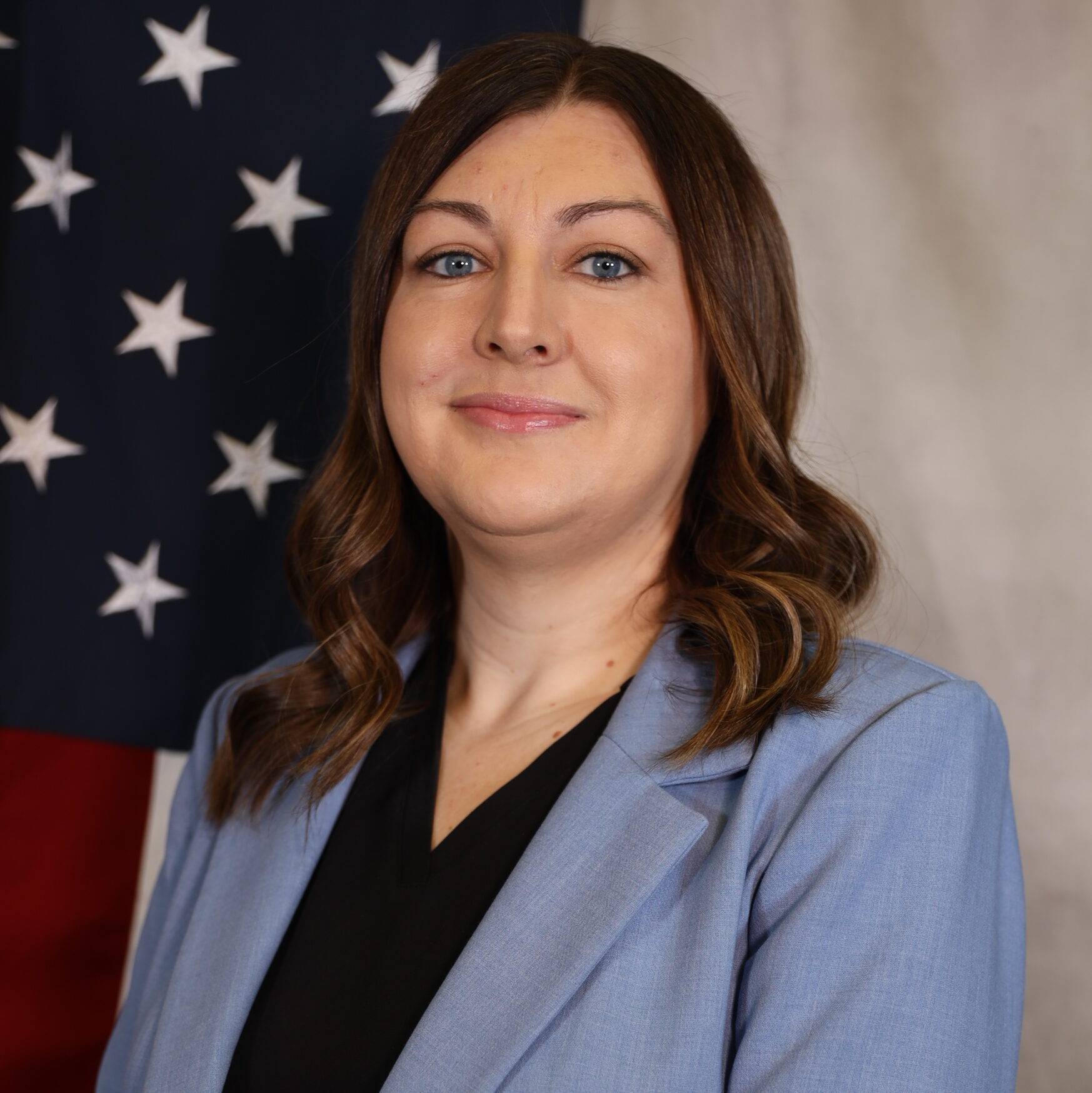 Sarah Manzanares in a blue blazer, standing before a U.S. flag.